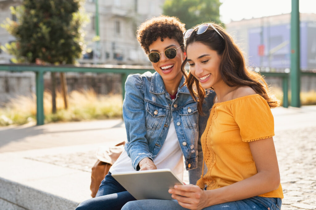 Two happy women using tablet outdoors