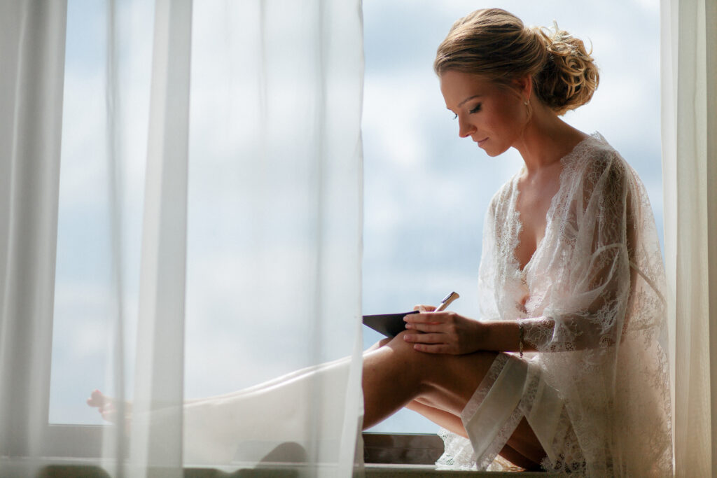 Bride in robe writing her custom wedding vows while sitting by a window